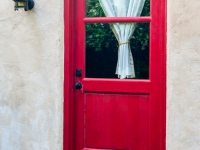 Red door with a curtain in the window on a house.