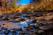 Flowing water over rocks with autumn leaves in a river.